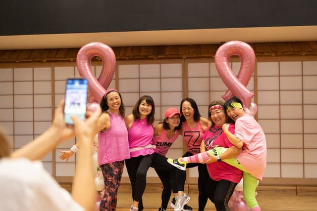 A group posing for a phone photo beside two giant pink ribbon balloons